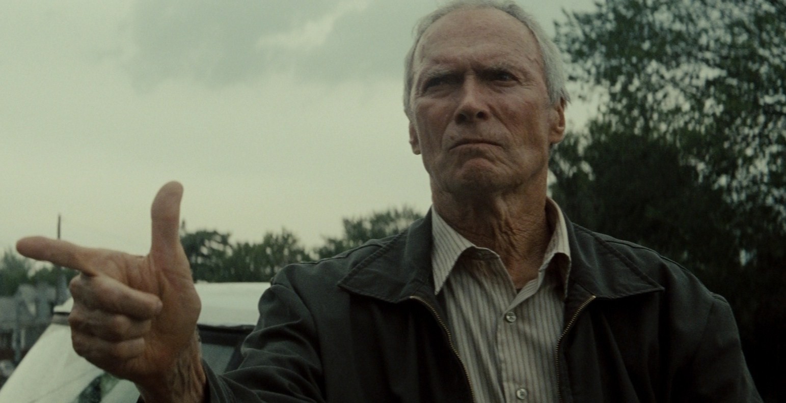Clint Eastwood in Gran Torino, in primo piano, mentre punta le dita a mo di pistola.